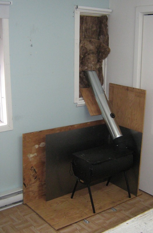 Portable wood stove inside house, with chimney exiting window.